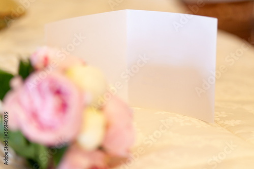 close-up of a blank white card and a bouquet of pink peonies out of focus on a white bedspread.