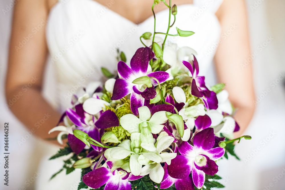 close-up bride in a white wedding dress holds a bouquet of purple and white orchids. The woman's face is not visible. girl is indoor. selective focus