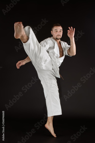 karate man training in-flight kick and posing on black background