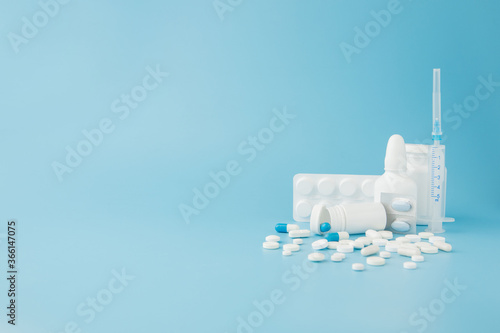 scattered variety pills, drugs, spay, bottles, thermometer, syringe and empty shopping trolley cart on blue background. pharmacy shopping concept