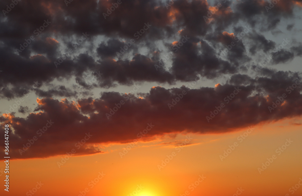 Obraz premium Summer sunset sky with orange and dark blue clouds