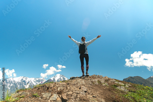 Young woman standing with raised hands with backpack on cliff's edge and looking into a wide valley. Hiking and travel in mountain © Leonid