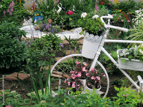 Old white bicycle decorated with flowers in the yard of the house. Garden decor