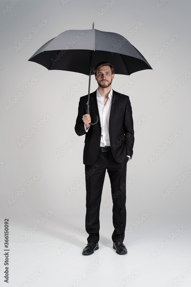 Businessman in a suit standing under black umbrella Businessman in a suit standing under black umbrella