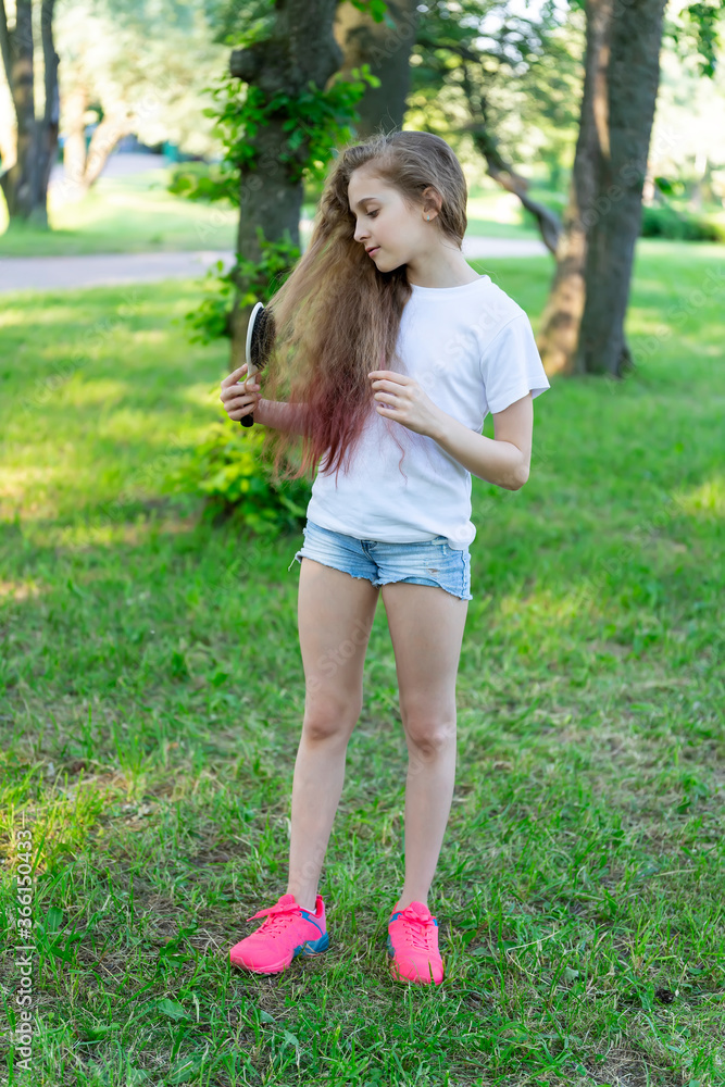 Little girl brushing her hair standing on the grass in the park against the trees. Little girl brushing her hair standing on the grass in the park against the trees.
