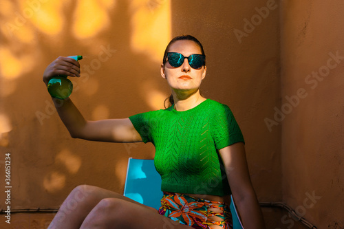 Woman in colorful beachwear sitting in backyard, holding spray bottle photo