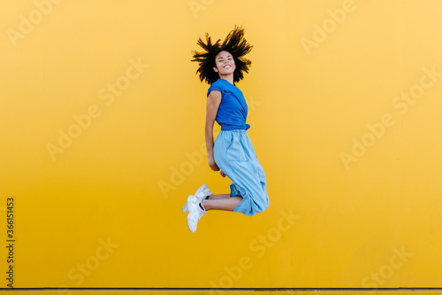 Pretty woman jumping for joy in front of yellow wall photo