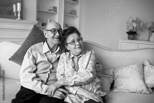 An elderly couple sit on the sofa and smile.