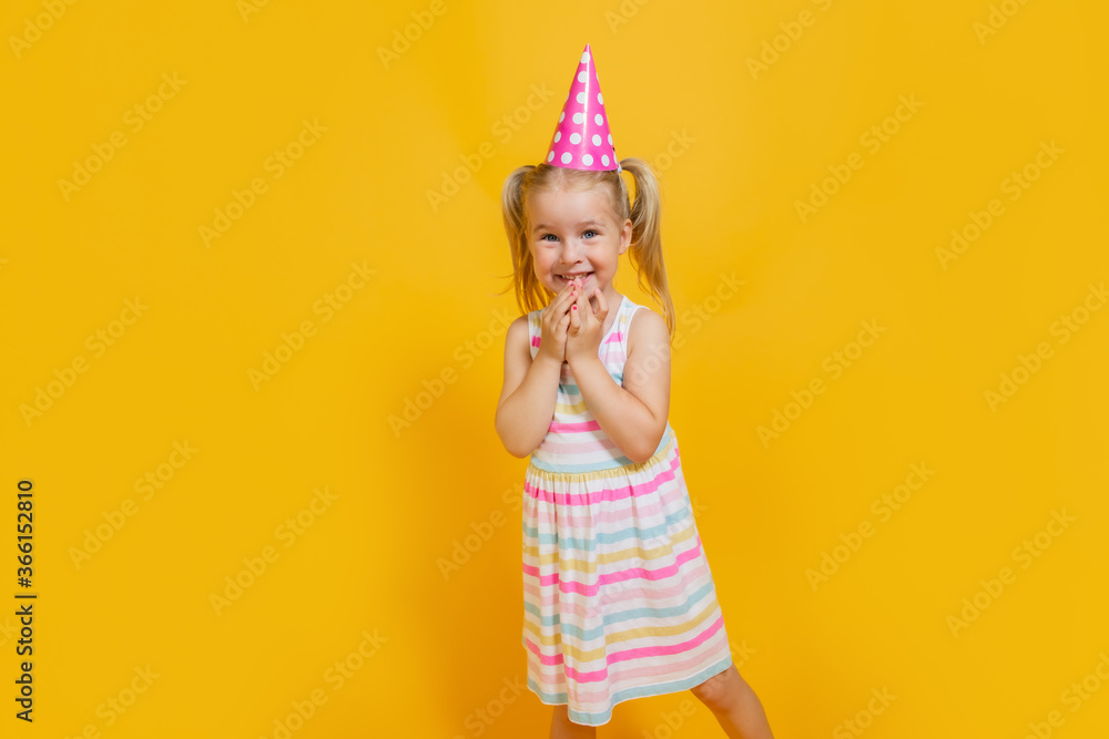 Happy birthday child girl with two ponytales in pink cap on colored yellow background. Copyspace. Happy birthday child girl with two ponytales in pink cap on colored yellow background. Copyspace.