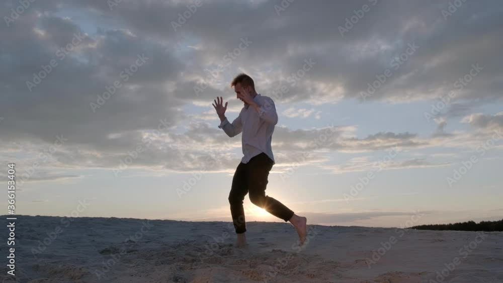 handsome dancer performs a freestyle dance composition on the sandy beach at sunset. Contemporary choreography. Slow motion footage. The live camera moves handsome dancer performs a freestyle dance composition on the sandy beach at sunset. Contemporary choreography. Slow motion footage. The live camera moves