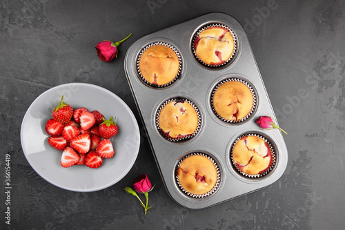 Homemade muffins with fresh strawberries, flat lay on dark concrete background