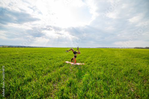 Beautiful young woman in a black top and shorts performs a handstand. A model stands on her hands, doing gymnastic splits against the blue sky. Healthy lifestyle concept