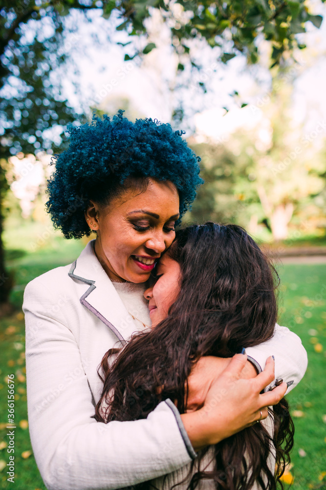 Loving mother with blue hair embracing daughter while standing in park Loving mother with blue hair embracing daughter while standing in park