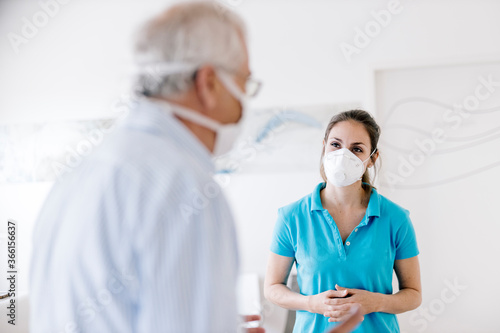 Senior man meeting his femal physiotherapist at the reception, wearing face masks photo