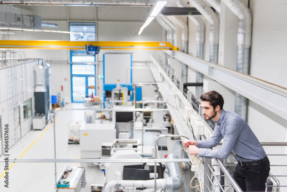 Young businessman standing on upper floor in a factory Young businessman standing on upper floor in a factory