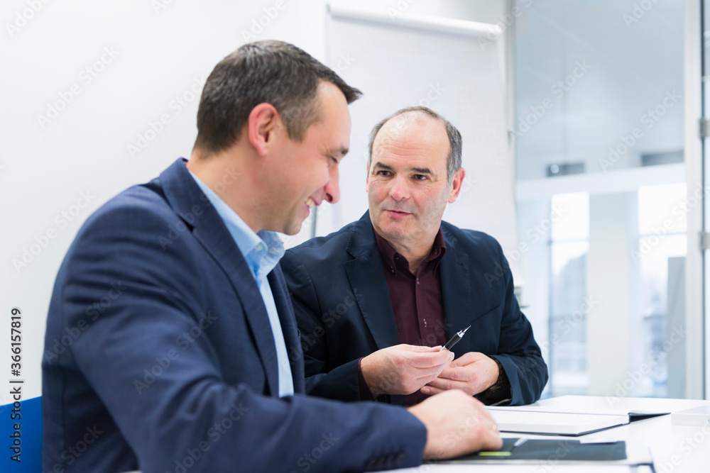 Two businessmen talking at desk in office Two businessmen talking at desk in office