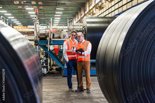 Two men in safety vests having a meeting in a rubber processing factory