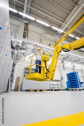 Man wearing hard hat standing on hoist in a factory photo