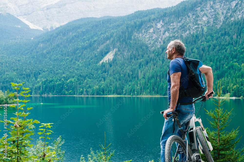 Senior man with e-bike enjoying view over Eibsee Senior man with e-bike enjoying view over Eibsee