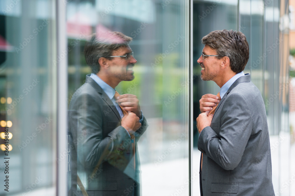 Businessman adjusting tie while looking at window in city Businessman adjusting tie while looking at window in city