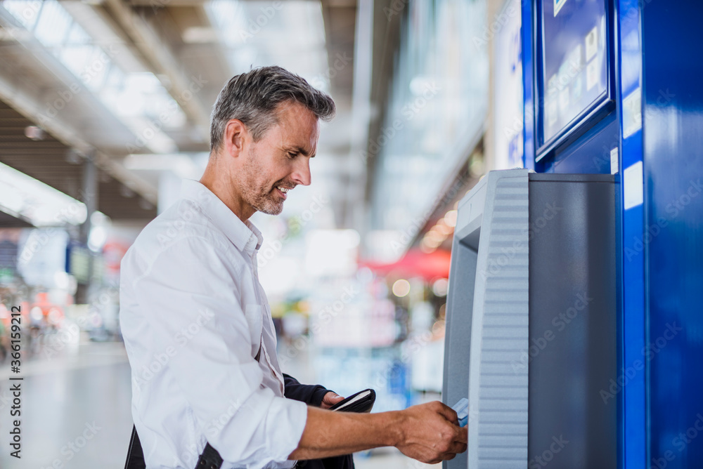 Businessman withdrawing money through ATM machine at railroad station Businessman withdrawing money through ATM machine at railroad station