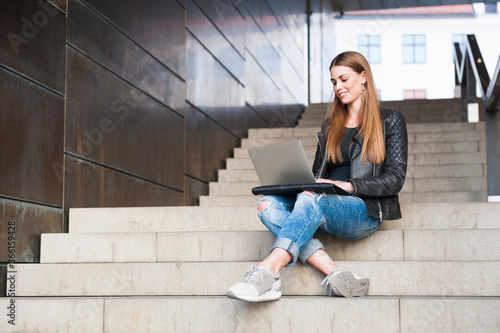 Happy young woman using laptop while sitting on steps in underground walkway