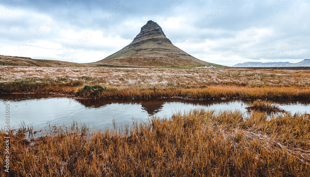 Fototapeta premium Scenic image of Iceland. The Kirkjufell volcano the coast of Snaefellsnes peninsula with overcast sky at Autumn time. Majestic Kirkjufell (Church mountain) the most famous icelandic landmark. Postcard