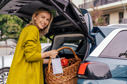 Portrait of happy woman with protective mask putting purchase in trunk of her car photo