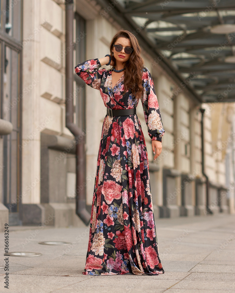 Pretty beautiful caucasian woman with long dark wavy hair wearing black and red colorful ball gown dress and sunglasses. Model standing and posing at city street Pretty beautiful caucasian woman with long dark wavy hair wearing black and red colorful ball gown dress and sunglasses. Model standing and posing at city street
