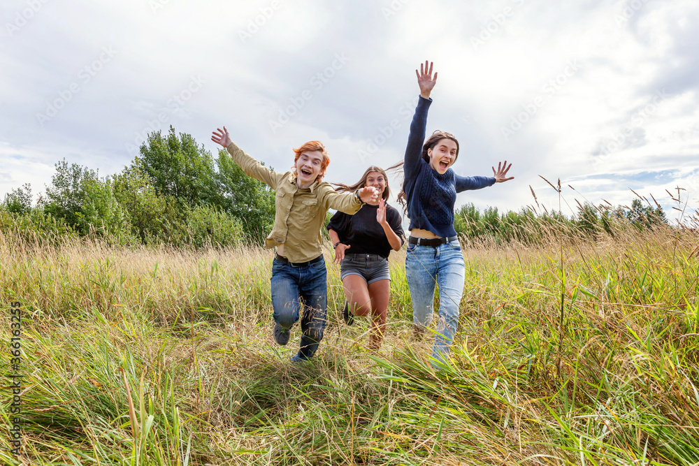 Summer holidays vacation happy people concept. Group of three friends boy and two girls running and having fun together outdoors. Picnic with friends on road trip in nature. Summer holidays vacation happy people concept. Group of three friends boy and two girls running and having fun together outdoors. Picnic with friends on road trip in nature.