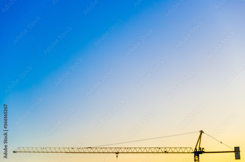 Construction crane on the background of the sunset sky. Blues, magenta and orange are saturated colors. Equipment for building houses. Place for text. Minimalism and nothing more. Construction crane on the background of the sunset sky. Blues, magenta and orange are saturated colors. Equipment for building houses. Place for text. Minimalism and nothing more.