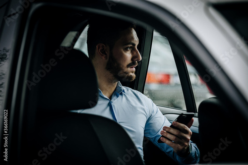 Handsome and formal looking man using his phone in the backseat of a car © Denis