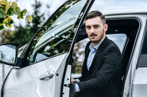 Formal looking man getting outside of his car wearing a suit