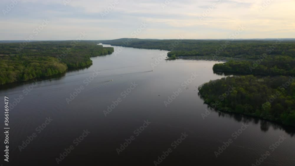 Aerial drone pan up and fly over large, blue lake with people and boats in Pennsylvania surrounded by green forest in the summer at sunset. Aerial drone pan up and fly over large, blue lake with people and boats in Pennsylvania surrounded by green forest in the summer at sunset.