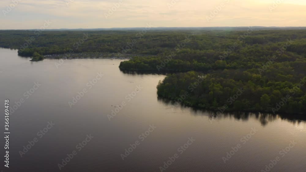 Aerial drone rotate and fly over large, blue lake with people and boats in Pennsylvania surrounded by green forest in the summer at sunset. Aerial drone rotate and fly over large, blue lake with people and boats in Pennsylvania surrounded by green forest in the summer at sunset.