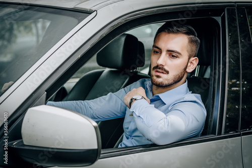 Handsome man sitting in luxury car fixing his shirt