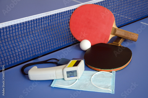 Table Tennis Paddles and ball on the blue table tennis table with medical mask and non-contact thermometer. Fitness during quarantine.