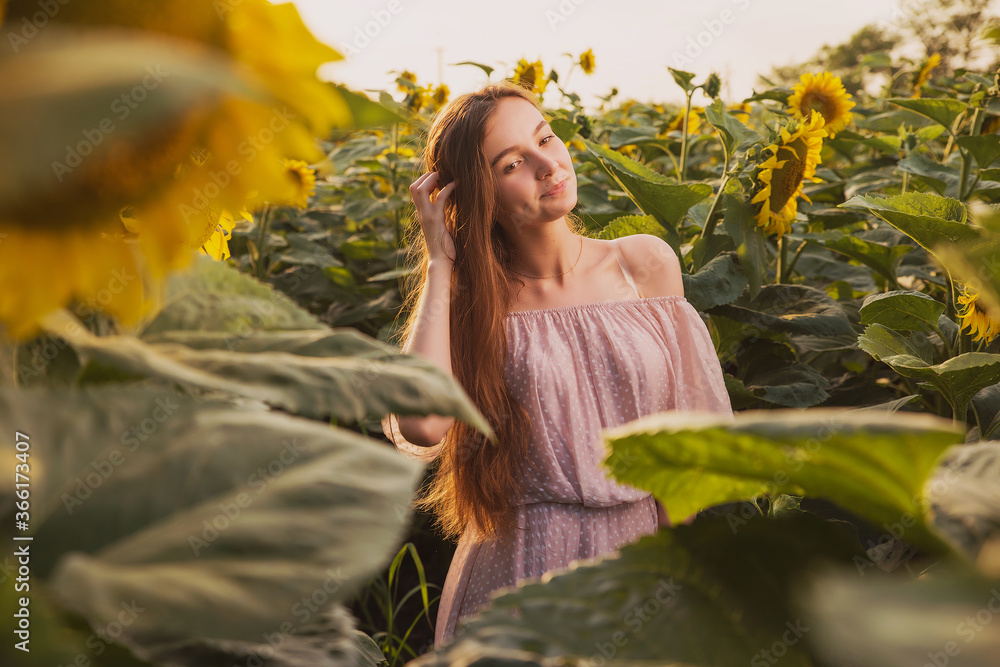 A Women in a short summer sundress poses against the background of a sunflower field, expressive and emotional summer portraits in the rays of the sunset on a background of flowers A Women in a short summer sundress poses against the background of a sunflower field, expressive and emotional summer portraits in the rays of the sunset on a background of flowers