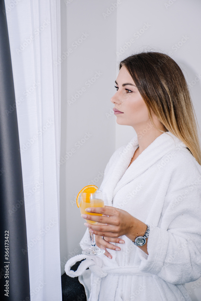 woman with a serious face looking at something while wearing a bathrobe and holding a glass of orange juice woman with a serious face looking at something while wearing a bathrobe and holding a glass of orange juice