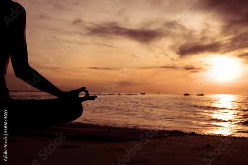 Silhouette of hand woman practicing yoga on the beach at sunset or sunrise. women do yoga. women exercising yoga in the beach.Young girl meditating in lotus posture.