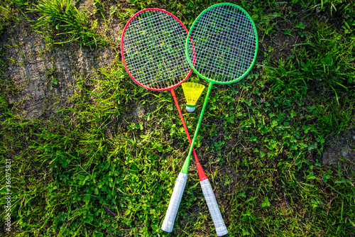 Two badminton rackets with a yellow shuttlecock on the green grass, summer active games