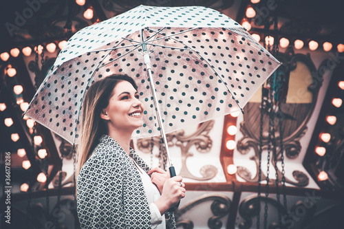 Cheerful woman looking at something and holding a dotted umbrella at a carnival