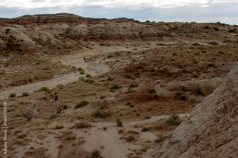 Distant female hiker walks along a dry river bed in the Bisti Badlands in the De-Na-Zin Wilderness in San Juan County, New Mexico Distant female hiker walks along a dry river bed in the Bisti Badlands in the De-Na-Zin Wilderness in San Juan County, New Mexico