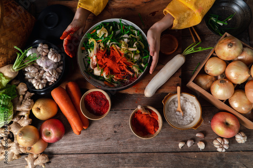 Asian women wearing Korean traditional costumes (hanbok) are mixing fresh stir-fry and kimchi ingredients with ingredients such as salt, garlic, gochugaru, fresh vegetables.