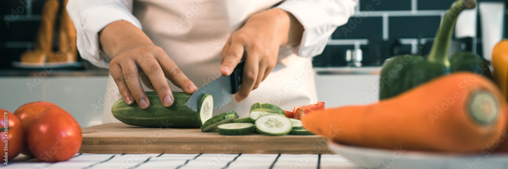 Housewife using knife and hands cutting cucumber on wooden board in kitchen room. Housewife using knife and hands cutting cucumber on wooden board in kitchen room.
