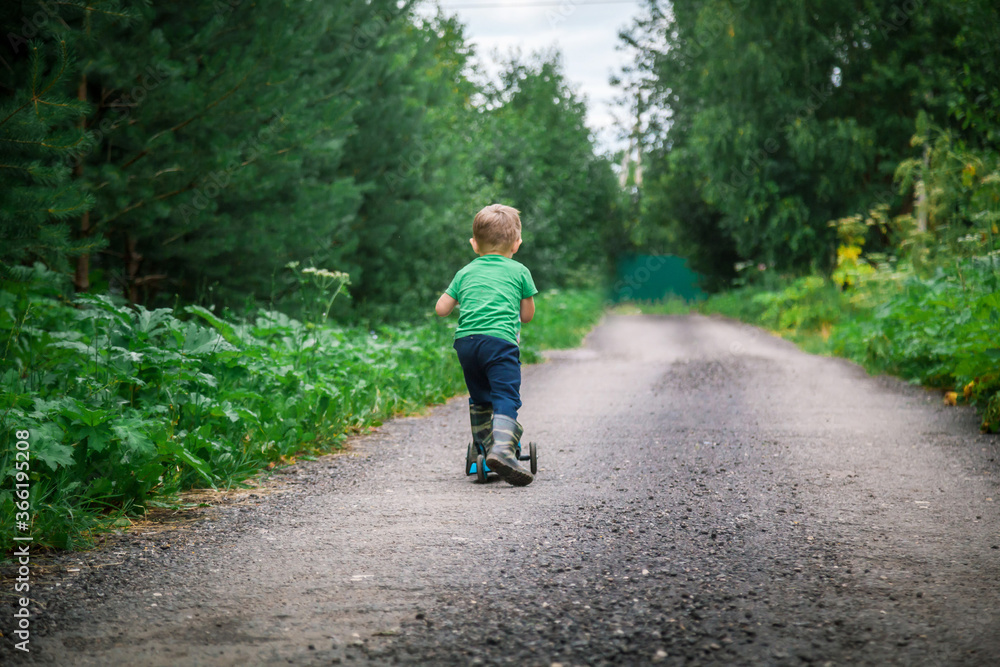 A little boy rides a scooter on a forest road.