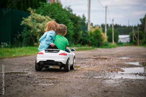 Little girl and boy riding a toy car.