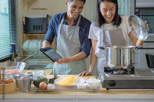 Happiness Asian couple using smart pad while cooking in kitchen together at home