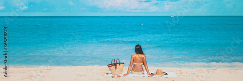 Beach summer vacation banner relaxing sunbathing woman lying on towel tanning alone panorama travel on blue ocean panoramic header crop.