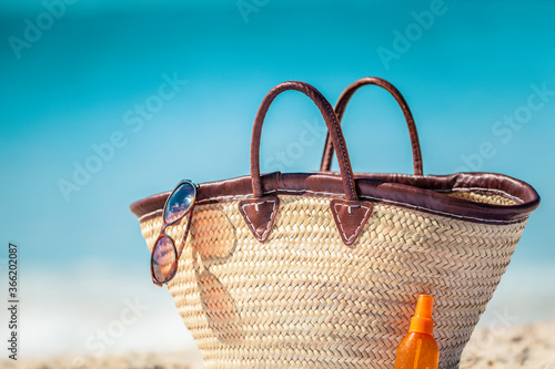 Summer vacation beach bag with sunglasses and sunscreen suntan bottle for solar protection skin care womens travel accessories for sun vacations.
